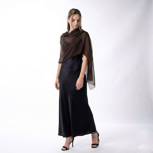 May include: A woman in a dark brown sheer shawl and a black satin maxi dress. The shawl is draped over the shoulders. The dress is a simple, elegant design. Black high-heeled sandals complete the outfit.