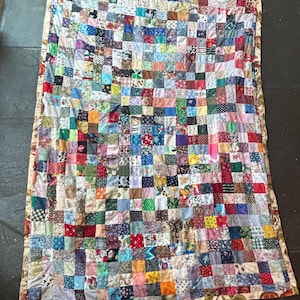 以下が含まれることがあります： さまざまな色と柄の小さな布の正方形を多数使用したパッチワークキルト。キルトは、花柄、幾何学模様、無地の生地が特徴です。端は模様入りのボーダーと吊り下げループで仕上げられています。