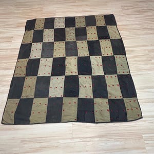 May include: A rectangular patchwork quilt featuring a repeating checkerboard pattern of alternating black and olive green fabric rectangles. Each individual fabric block is accented with small, hand-stitched red thread tufts distributed across the surface.