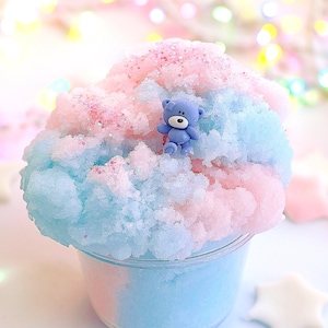 May include: Blue and pink fluffy slime with a small blue teddy bear charm in the center. The slime is in a clear plastic container.