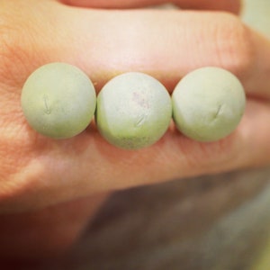 May include: Three round, light green beads with a smooth, matte finish.