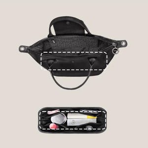 May include: Black handbag with top handles, open to reveal the interior. A separate black organizer is shown below, filled with cosmetics and personal items. The bag has a zipper closure and a small silver charm.