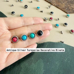 Könnte beinhalten: Eine Sammlung von dekorativen Nieten aus antikem Silber mit runden, glatten Cabochon-Steinen in Türkis, Pink und Schwarz. Jede Niete ist von einem gedrehten Metallrand umgeben, wobei mehrere lose Nieten auf der Oberfläche verstreut sind.