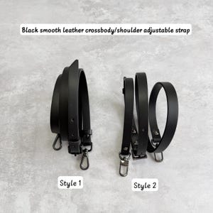 May include: Two black smooth leather adjustable crossbody or shoulder straps. Style 1 features a buckle and lobster clasps. Style 2 features a buckle and lobster clasps. The text reads: Black smooth leather crossbody/shoulder adjustable strap.