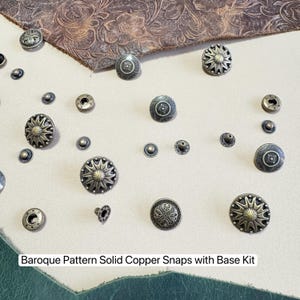 Könnte beinhalten: Eine Auswahl an antik kupferfarbenen Druckknöpfen mit Barockmuster, in verschiedenen Größen und Stilen. Das Bild zeigt auch ein Stück braunes Leder mit floralem Design. Der Text unten lautet "Baroque Pattern Solid Copper Snaps with Base Kit."