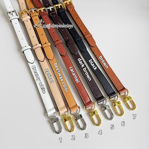 Puede incluir: Siete correas de cuero de diferentes colores con herrajes dorados. Las correas están etiquetadas con sus colores: blanco cremoso, albaricoque, color cera de abejas, caramelo, marrón oscuro, negro y marrón.