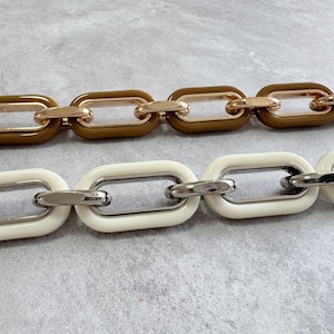 Może przedstawiać: Zbliżenie dwóch naszyjników z ogniwami łańcucha. Jeden łańcuch ma brązowe ogniwa ze złotymi łącznikami. Drugi łańcuch ma białe ogniwa ze srebrnymi łącznikami. Ogniwa mają owalny kształt.