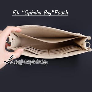 Puede incluir: Una bolsa de cuero beige con varios compartimentos y un cierre de metal dorado. La bolsa está abierta y el interior es visible. El texto "Fit "Ophidia Bag" Pouch" está impreso sobre un fondo blanco encima de la bolsa.