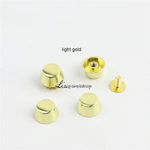 May include: Light gold metal bag feet and screw-back studs. The image shows four cone-shaped feet, one screw-back stud, and a cup-shaped stud. The text "light gold" is visible in the image. The brand name "Lia simpledesign" is also visible.