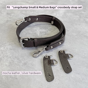 May include: A mocha leather crossbody strap set with silver hardware. The set includes a main strap with a buckle and two smaller connector pieces. The text on the image reads: Fit "Longchamp Small & Medium Bags" crossbody strap set.
