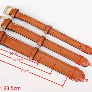 May include: Three tan watch straps with gold-tone metal buckles. The straps have varying widths of 1.5 cm, 1.8 cm, and 2.5 cm. The total length of the straps is 23.5 cm, with adjustment hole positions marked at 11 cm, 14.5 cm, and 18 cm.