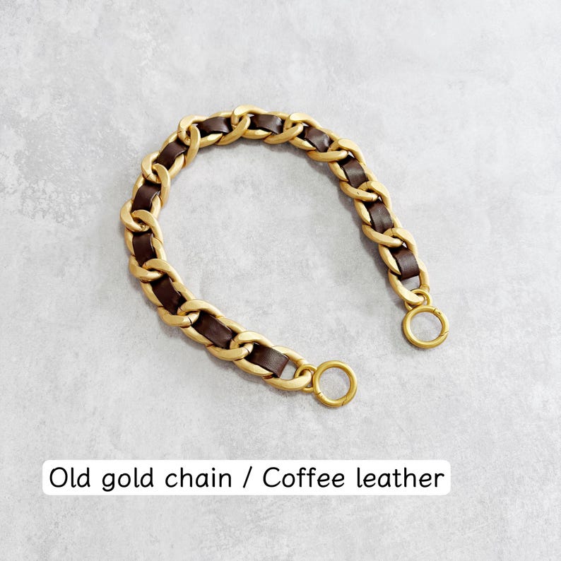 Peut inclure: Une sangle en cha&icirc;ne incurv&eacute;e compos&eacute;e de maillons en m&eacute;tal dor&eacute; mat entrelac&eacute;s de bandes de cuir marron caf&eacute;. Les extr&eacute;mit&eacute;s de la cha&icirc;ne se terminent par deux anneaux circulaires en m&eacute;tal dor&eacute;. Le texte indique : Old gold chain / Coffee leather.