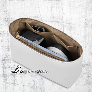 May include: White leather handbag organiser with multiple compartments and pockets. The organiser is filled with various items, including a phone, a wallet, and a small cosmetic bag. The organiser is labelled "Lia.simpledesigns".