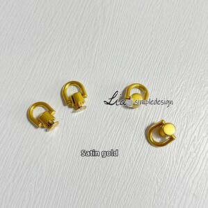 以下が含まれることがあります： サテン仕上げの金色の金属製のDリング金具が3つ。リングの直径は約1cmです。画像にはLia's Simple Designと書いてあります。