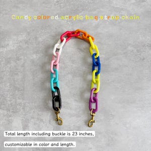 May include: A colorful acrylic bag strap chain with a total length of 23 inches. The chain features links in various colors, including red, orange, yellow, blue, and purple. The text "Candy colored acrylic bag strap chain" is at the top. The text "Total length including buckle is 23 inches, customizable in color and length" is at the bottom.