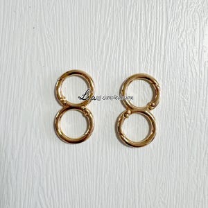 May include: Two gold-toned metal key rings with two loops each. The key rings are designed to be used for attaching keys, bags, or other items.