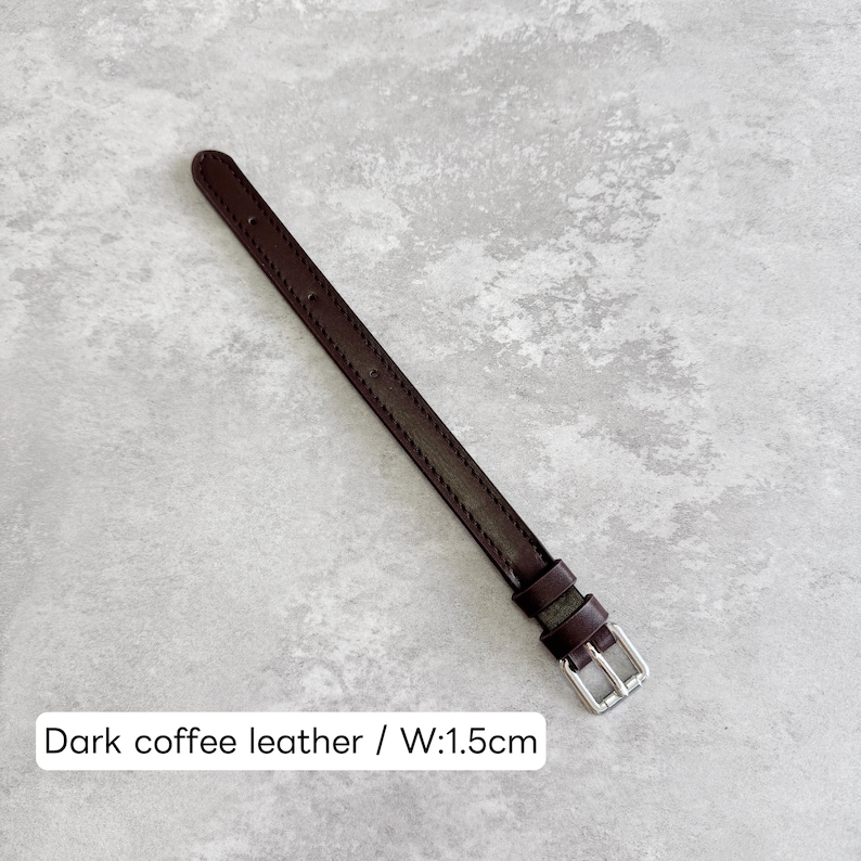 May include: A dark coffee brown leather watch strap featuring tonal stitching along the edges, two leather keepers, and a silver-toned metal buckle. The strap has a width of 1.5 cm as indicated by the text overlay on the image.