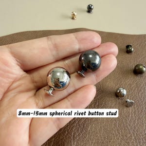 May include: Two spherical rivet button studs with a metallic finish, one silver and one dark grey, featuring a screw-back mechanism. The text 8mm-15mm spherical rivet button stud is visible. These metal fasteners have a smooth, rounded surface.