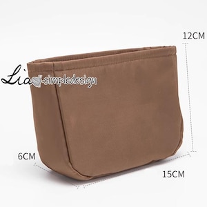 Könnte beinhalten: Eine braune Stofftasche mit Reißverschluss. Die Tasche ist 12 cm lang, 6 cm breit und 15 cm hoch.