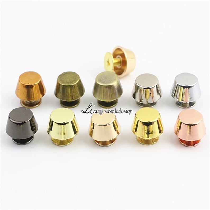 May include: A selection of ten metal cone-shaped studs in diverse metallic finishes, including gold, silver, bronze, and black. Each stud features a flat base and a screw for attachment. The studs are arranged on a white surface.