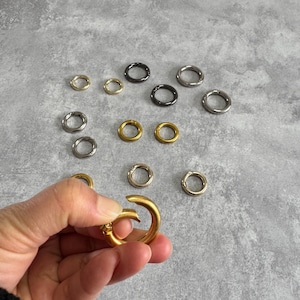 May include: Assortment of metal rings in gold, silver, and black finishes. The rings are of various sizes and are ideal for attaching to bags, keychains, or other accessories.