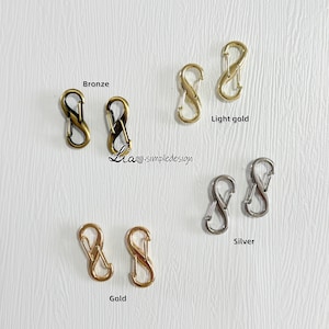 May include: Two sets of gold, bronze, light gold, and silver infinity shaped clasps. The clasps are arranged in rows with the text "Bronze", "Light gold", "Silver", and "Gold" below each row.