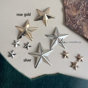 May include: A close-up of two sets of star-shaped metal embellishments. The larger stars are available in rose gold and silver. The smaller stars are silver and are scattered around the larger stars. The text "rose gold" and "silver" are written on the image.