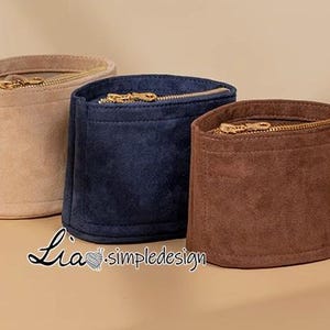 Puede incluir: Tres bolsas de fieltro con cremallera en beige, azul marino y marrón. Las bolsas están alineadas en una fila de izquierda a derecha.