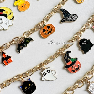 Op de afbeelding: Een goudkleurige metalen kettingarmband met diverse Halloween-emaille bedels, waaronder pompoenen, geesten, een zwarte vleermuis, een heksenhoed met de tekst Wizard in Training en een zwarte kat. De tekst Lia simpledesign is zichtbaar.