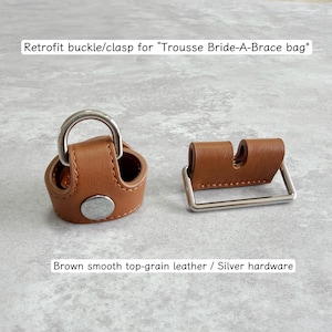 Może przedstawiać: Brązowy skórzany zestaw klamry i zapięcia ze srebrnym osprzętem. Zaprojektowany do torby "Trousse Bride-A-Brace". Klamra ma D-ring, a zapięcie jest prostokątne.
