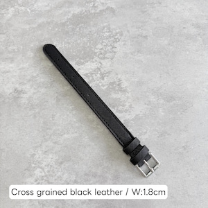 May include: A cross-grained black leather watch strap featuring a silver-toned metal buckle and two matching leather keepers. The strap has a width of 1.8 cm as indicated by the text. The surface of the leather displays a fine, textured pattern.