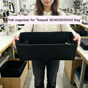 Puede incluir: Organizador de fieltro negro para bolso, sostenido por una persona. El organizador tiene múltiples compartimentos y un cierre de cremallera. El texto en la imagen dice: Organizador de fieltro para "Keepall 35/45/50/55/60 Bag".