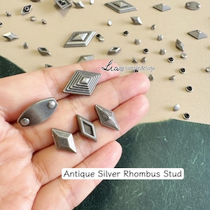 Peut inclure: Divers clous en argent antique en forme de losange, de différentes formes et tailles, dont des diamants et des ovales. Les clous ont un aspect vintage et vieilli. Le texte "Antique Silver Rhombus Stud" est visible.