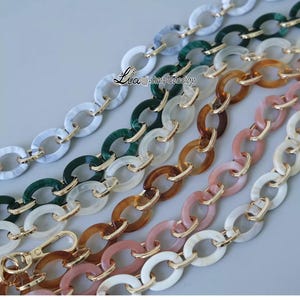 Pode incluir: Cinco elos de corrente de pl&aacute;stico de diferentes cores com detalhes dourados. As correntes s&atilde;o de v&aacute;rias cores, incluindo branco, verde, marrom, rosa e uma cor marrom claro. As correntes s&atilde;o todas de forma oval e t&ecirc;m um conector de metal dourado no centro de cada elo.