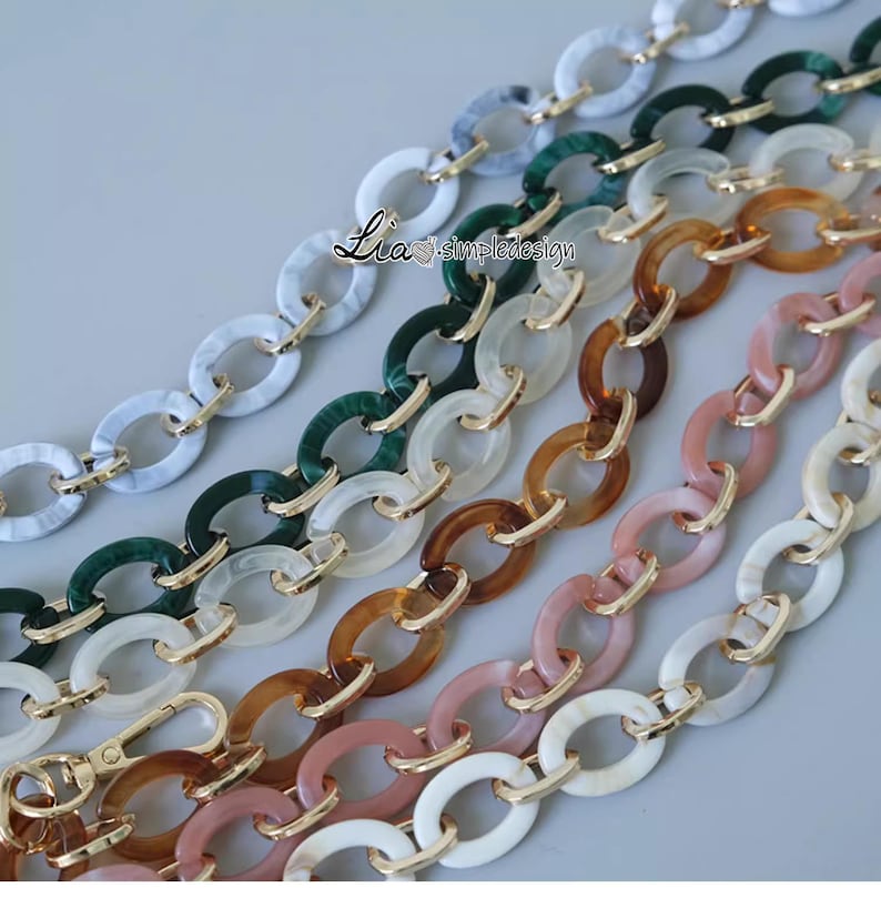 Pode incluir: Cinco elos de corrente de pl&aacute;stico de diferentes cores com detalhes dourados. As correntes s&atilde;o de v&aacute;rias cores, incluindo branco, verde, marrom, rosa e uma cor marrom claro. As correntes s&atilde;o todas de forma oval e t&ecirc;m um conector de metal dourado no centro de cada elo.