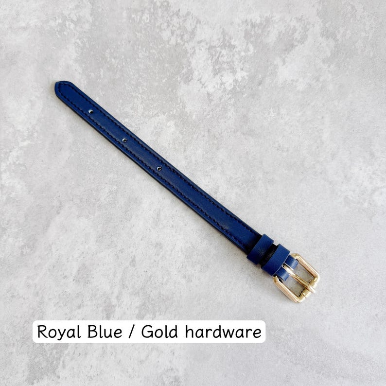 May include: A royal blue strap featuring gold-toned metal hardware, including a buckle and two loops. The strap has a series of evenly spaced holes for adjustment. The text "Royal Blue / Gold hardware" is printed at the bottom of the image.