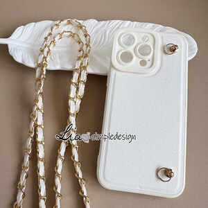 May include: White iPhone case with a gold chain strap. The case has a textured surface and gold accents. The chain strap is white with gold links. The text "Lia simpledesign" is visible on the image.