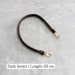 May include: Dark brown braided handbag strap with gold-coloured clasps. The strap is 69 cm (27 inches) long. The image shows the strap against a grey background.