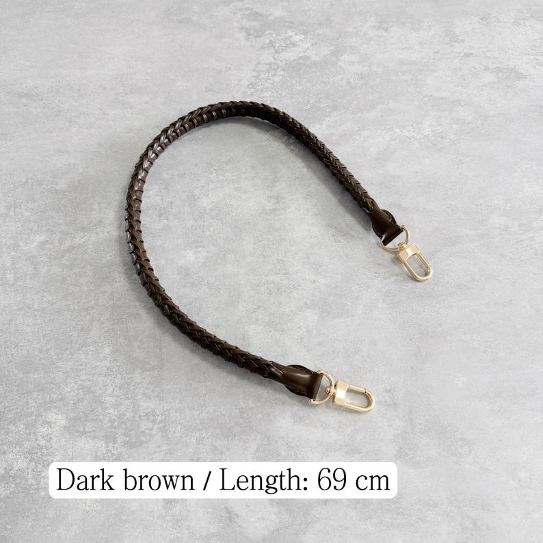 May include: Dark brown braided handbag strap with gold-coloured clasps. The strap is 69 cm (27 inches) long. The image shows the strap against a grey background.