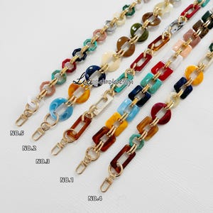 May include: Five decorative bag straps featuring interlocking resin links in various colours and patterns, connected by gold-tone metal rings. Each strap includes a gold-tone lobster clasp at the end. The text Lia simpledesign is visible.