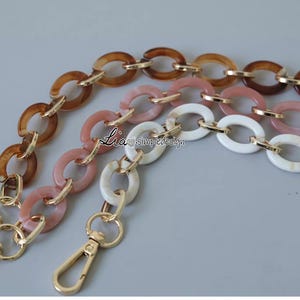 Pode incluir: Uma corrente multicolorida com elos ovais marrons, rosa e brancos. A corrente tem um fecho dourado.