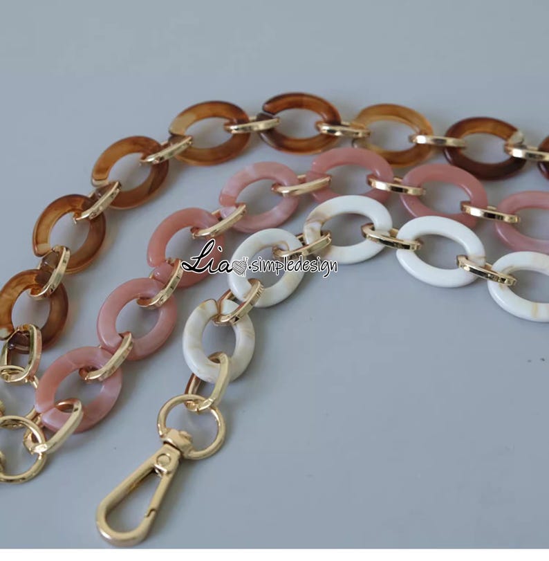 Pode incluir: Uma corrente multicolorida com elos ovais marrons, rosa e brancos. A corrente tem um fecho dourado.
