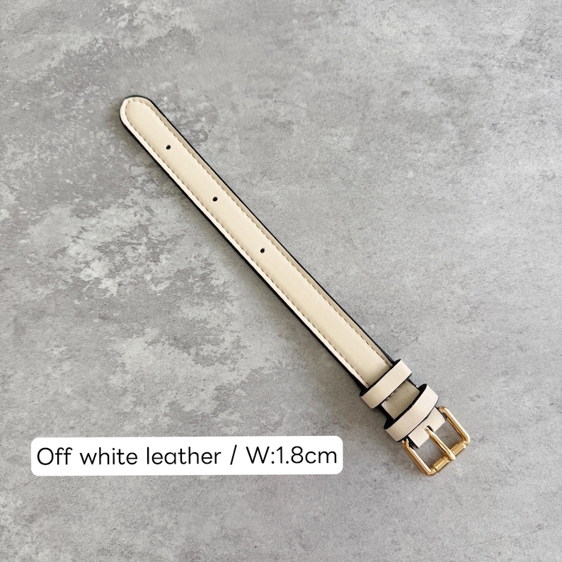 May include: An off-white leather watch strap featuring a gold-tone metal buckle and two matching keepers. The strap includes several adjustment holes and is labeled with the text Off white leather / W:1.8cm, indicating a width of 1.8 cm.