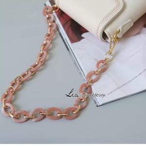 Pode incluir: Uma al&ccedil;a de corrente para bolsa rosa e dourada com elos ovais. A al&ccedil;a &eacute; feita de pl&aacute;stico e metal.