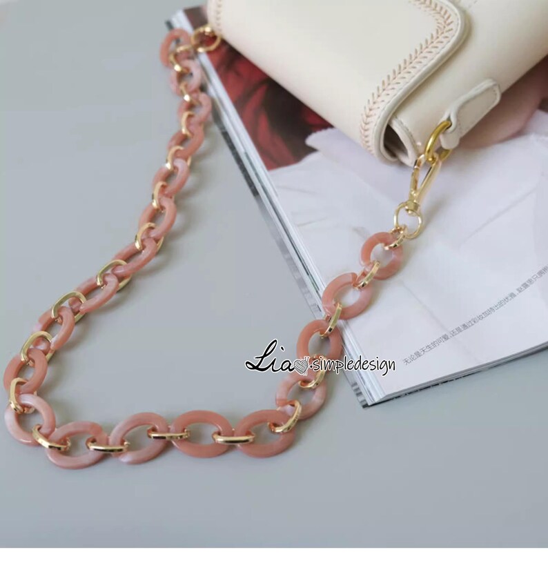 Pode incluir: Uma al&ccedil;a de corrente para bolsa rosa e dourada com elos ovais. A al&ccedil;a &eacute; feita de pl&aacute;stico e metal.