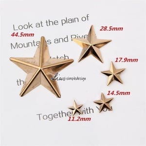 May include: Four gold-toned metal star shapes of varying sizes. The largest star is 44.5 mm, the next largest is 28.5 mm, the next is 17.9 mm, and the smallest is 14.5 mm. The stars are on a white background.