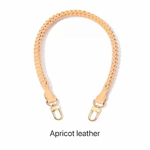 May include: Apricot leather handbag strap with a braided design. The strap has gold-coloured metal clasps on each end. The text "Apricot leather" is below the strap.