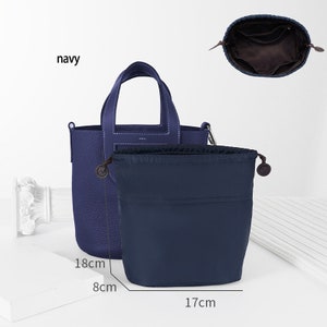 May include: A navy blue leather tote bag with a top handle and a zip closure. The bag is 18 cm tall, 8 cm wide, and 17 cm deep. It comes with a matching navy blue drawstring pouch.