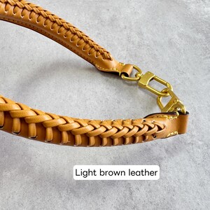 May include: Close-up of a light brown leather handbag strap with a braided design. The strap has gold-coloured metal hardware and the text "Light brown leather". The strap is likely for a purse or tote bag.