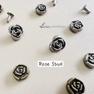 May include: An assortment of rose-shaped metal studs in silver and antique gold finishes. The studs are arranged on a light surface. The image includes the text "Rose Stud" and the brand name "Lia simpledesign".